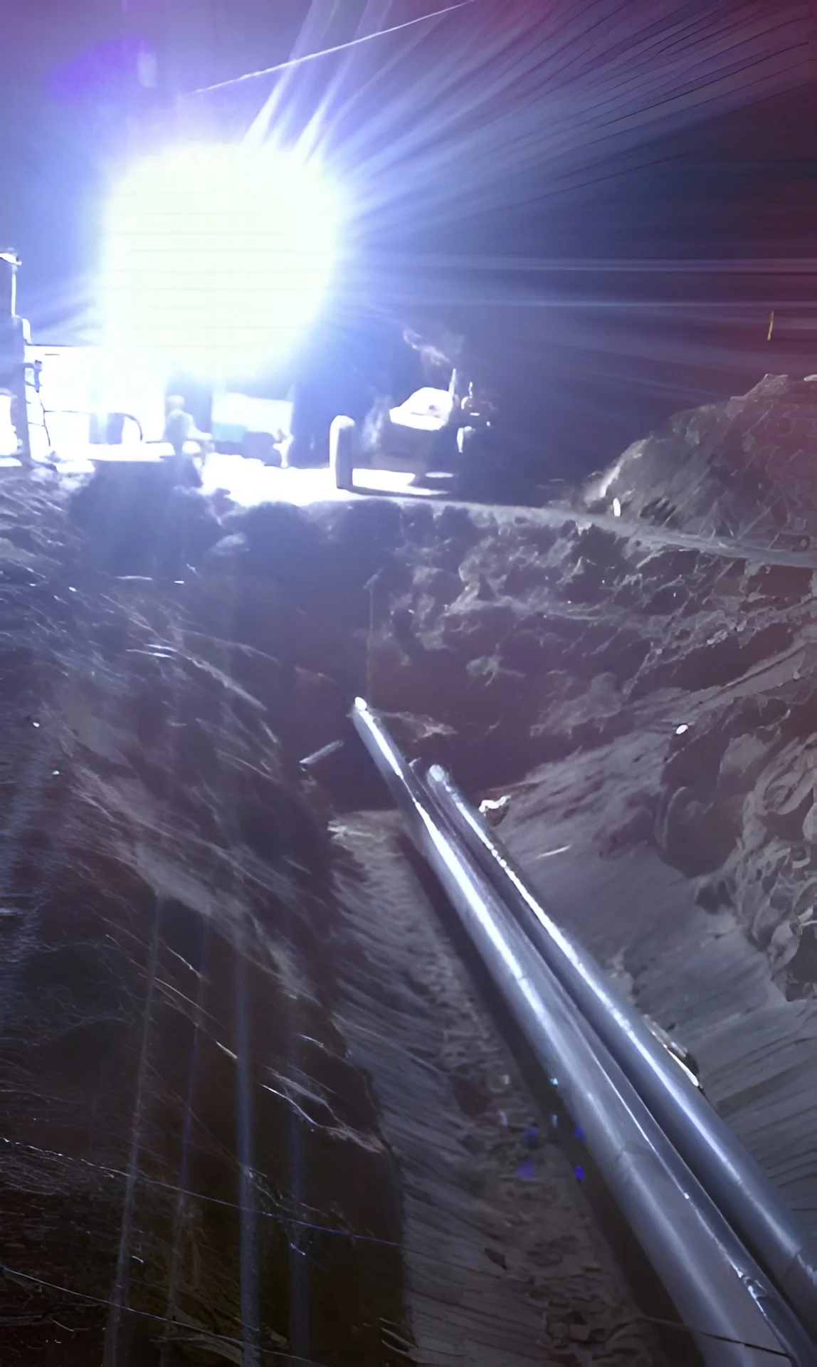 Night excavation with crew laying underground pipe under work-light glare
